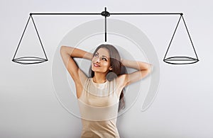 Thinking beautiful woman looking up on the scale above the head and weigh the pros and cons on grey background. Business concept