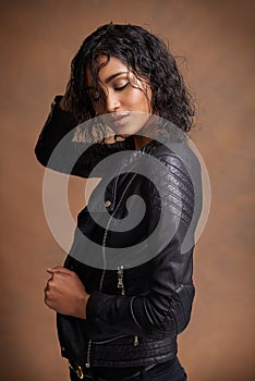 Thinking, beauty and woman with fashion, leather jacket and confident girl on a brown studio background. Stylish clothes