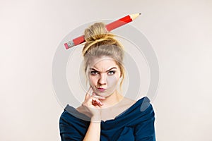 Thinking blonde woman having big pencil in hair