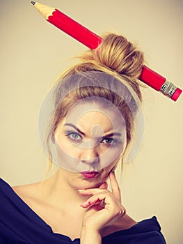 Thinking blonde woman having big pencil in hair