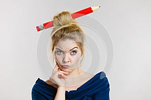 Thinking blonde woman having big pencil in hair