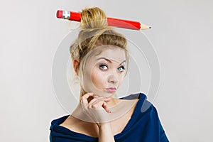 Thinking blonde woman having big pencil in hair