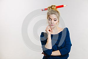 Thinking blonde woman having big pencil in hair