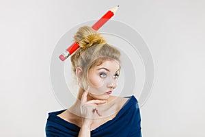 Thinking blonde woman having big pencil in hair