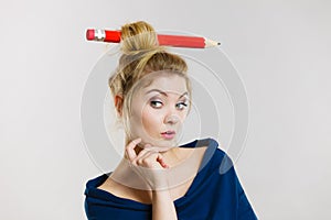 Thinking blonde woman having big pencil in hair