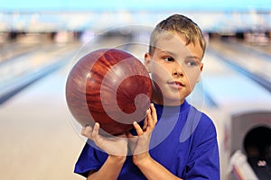 Thinking boy holds ball in bowling