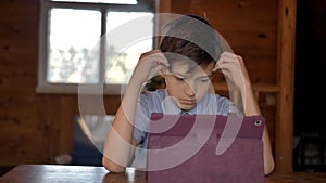 Thinking boy at the table near the tablet clutching his head