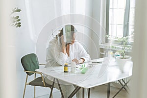 Thinking brunette woman doctor nutritionist plus size in white shirt working on table with house plant in bright modern office