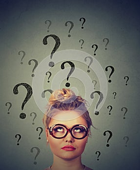 Thinking business woman with glasses looking up at many questions marks above head