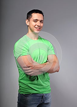 Thinking casual happy smiling young man with folded arms in green t-shirt on grey backgrond