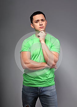 Thinking casual young man with green shirt and blue jeans on grey backgrond