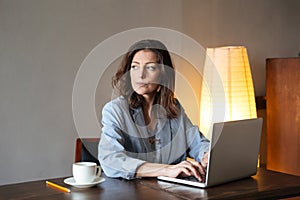 Thinking concentrated woman writer sitting indoors using laptop