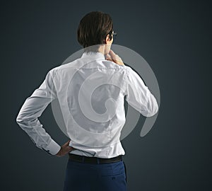 Thinking concept with pensive businessman in white shirt and glasses standing on abstract black wall background