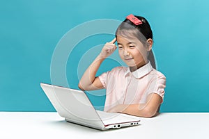 Thinking, Cute asia little girl who enjoy the laptop computer on blue background