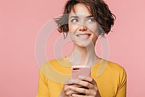 Thinking dreaming young beautiful woman posing isolated over pink wall background using mobile phone