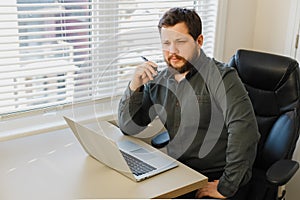 Thinking enterpreneur sitting with pen and laptop at cabinet.