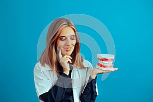 Thinking Female Dentist Holding a plastic Denture Model