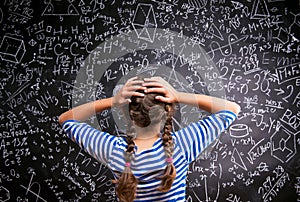 Thinking girl holding head against big blackboard, back view