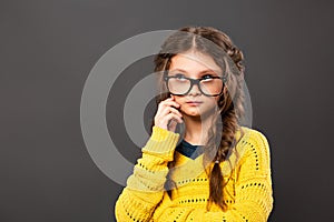 Thinking grimacing serious schoolgirl in eyeglasses looking up on grey studio background. Back to school. The concept of education