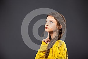 Thinking grimacing serious schoolgirl looking up on grey studio background. Back to school. The concept of education