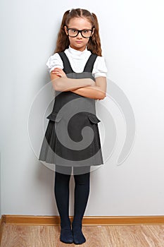 Thinking happy smiling pupil girl in fashion eyeglasses with folded arms in school uniform