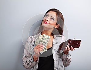 Thinking happy woman holding dollars and wallet in hands and wan