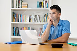 Thinking hispanic hipster man stay at home and work with concentration at computer