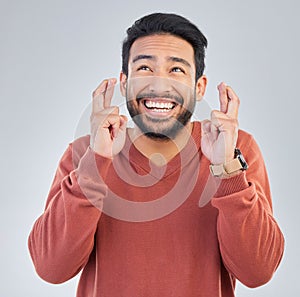 Thinking, luck and hand gesture with a man in studio on a gray background praying in hope of a miracle. Idea, smile and