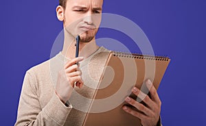 Thinking man with a brown paper notebook looks at page photo