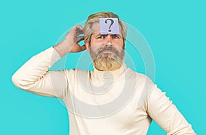 Thinking man with question mark on blue background. Man with question mark on forehead. Paper notes with question marks. Beard man