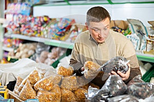 Thinking man stands in department of supermarket and chooses packaged raisins