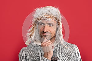 thinking mature guy portrait. man in earflap hat. grizzled guy in sweater on red background.