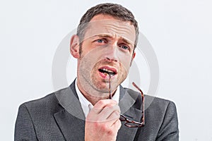 Thinking middle aged businessman biting his eyeglasses expressing doubt