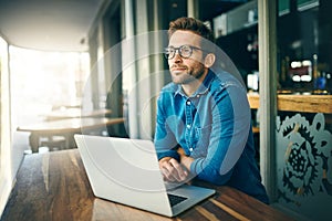 Thinking of my next move. a handsome young businessman sitting alone and looking contemplative while using his laptop in