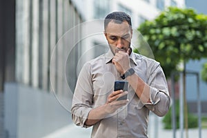 Thinking and sad muslim businessman reading message from smartphone, man outside office building using phone depressed