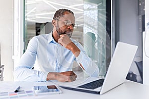 Thinking serious African American businessman working inside office, successful business man boss looking at laptop