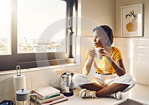 Thinking, serious and African woman drinking coffee while sitting on the kitchen counter alone at home. One content