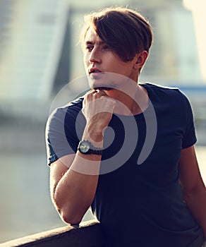 Thinking serious handsome young man looking on city center background with fashion watch on the hand. Closeup toned color portrait