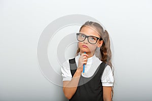 Thinking serious skeptical pupil girl in fashion eyeglasses with in school uniform with pencile inder the face