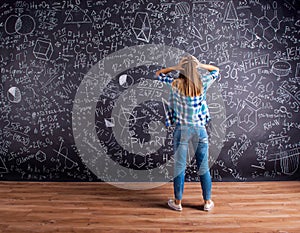 Thinking student holding head against big blackboard, back view