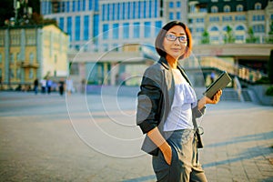 Thinking stylish asian businesswoman holding a tablet pc outdoors.