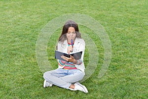 thinking teen child making notes in notebook sitting on grass. taking notes. student make notes