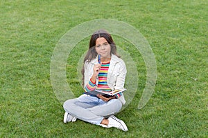 thinking teen girl making notes in notebook sitting on grass. taking notes. student make notes.