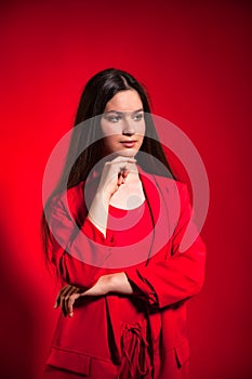 Thinking teen girl wearing stylish red costume over red background wall looking away