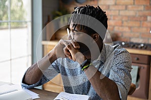 Pensive african male student sit at table reflect on task