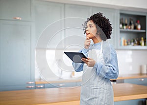 thinking woman in apron with tablet pc in kitchen