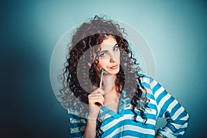 Thinking. woman with curly hair thinking holding pen on cheek looking at you skeptically