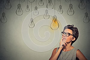 Thinking woman in glasses looking up with light idea bulb above head