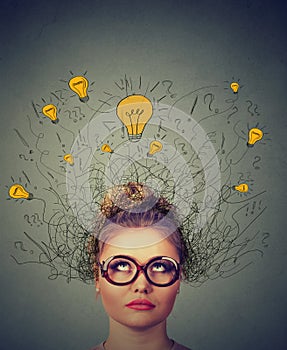 Thinking woman in glasses with question signs and light idea bulb above head looking up wondering