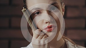 Thinking woman holding money stack near face and looking into camera